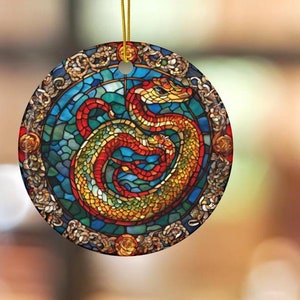 May include: A round ceramic ornament with a stained glass design of a red and gold dragon. The dragon is curled up in a circle and has a detailed mosaic pattern.