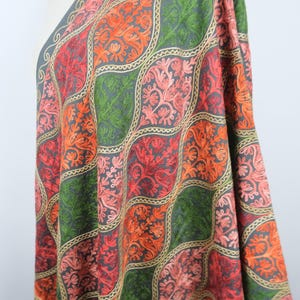 May include: A dark gray shawl featuring an intricate, repeating pattern of embroidered ogee shapes. The embroidery consists of vibrant orange, red, and green floral motifs outlined in light tan thread, creating a textured, colorful surface.