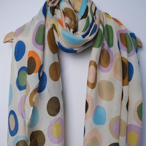 May include: A white scarf with a colorful polka dot pattern. The dots are various shades of blue, green, orange, brown, pink, and yellow.