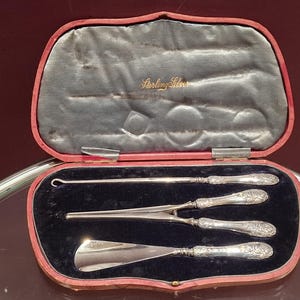 May include: An antique sterling silver surgical instrument set in a red leather case with a blue velvet interior. The case is open, showing three instruments with decorative handles. The case is labelled "Sterling Silver".