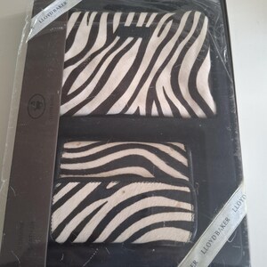 May include: A boxed set containing a wallet and a clutch, both with a zebra stripe design. The black and white pattern is on a textured surface. The set is presented in a black box, with the brand name "Lloyd Baker" visible.