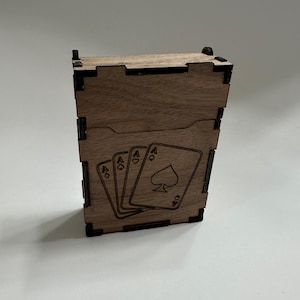 Peut inclure: Une boîte en bois pour cartes à jouer avec un motif gravé au laser de cartes à jouer. Le motif présente l'As de Pique et trois As de Cœur et de Carreau. La boîte est en bois brun clair avec des coins noirs.