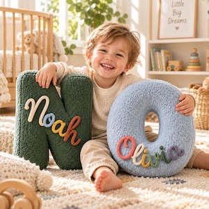 May include: A dark green textured letter N cushion with the name Noah in colourful yarn lettering and a light blue textured letter O cushion with the name Olivia in colourful yarn lettering, both featuring soft, plush, sherpa-like fabric construction.