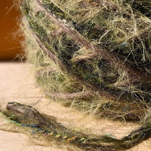 Peut inclure: Une pelote de fil vert avec de longues fibres duveteuses. Le fil a un léger éclat et est enroulé en boule.