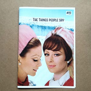 May include: A magazine cover featuring two women with vintage hairstyles and pearl earrings. The cover has the text "THE THINGS PEOPLE SAY" and the number "#19" in the upper right corner. The background shows a snowy mountain scene.