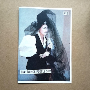 May include: A magazine cover featuring a person in a black outfit and veil. The person is wearing a white blouse with large sleeves. The text "THE THINGS PEOPLE SAY" is at the bottom of the cover, with the number "#18" in the top right corner.