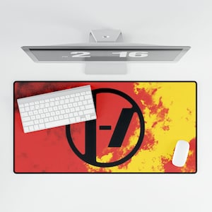 May include: A rectangular desk mat with a red and yellow background, a black circle with a slash and a dash, a white keyboard, and a white mouse. The desk mat is under a computer monitor.