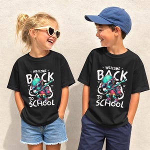 May include: Two black t-shirts featuring a graphic of a green alien wearing sunglasses and a backpack, dabbing. The text reads "WELCOME BACK TO SCHOOL" in white lettering. The shirts are worn with blue denim shorts and a blue baseball cap.