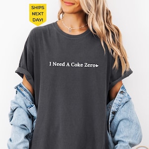 May include: A dark gray t-shirt with the text "I Need A Coke Zero" in white with a small heart symbol.