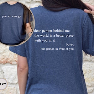 May include: Navy blue t-shirt with the text "you are enough." on the front and the text "dear person behind me, the world is a better place with you in it. love, the person in front of you" on the back.