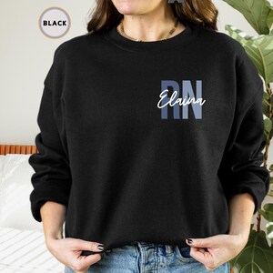 May include: Black sweatshirt with a blue and white gradient design that says "RN Elaina" on the front.
