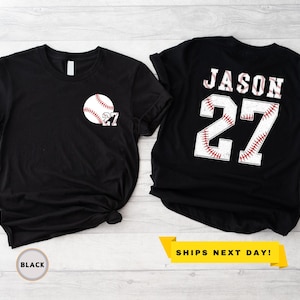 May include: Two black t-shirts. One features a baseball graphic with the number 27 on the front. The other shirt displays the name "JASON" and the number 27 on the back, with a baseball stitch design. The text "SHIPS NEXT DAY!" is also visible.