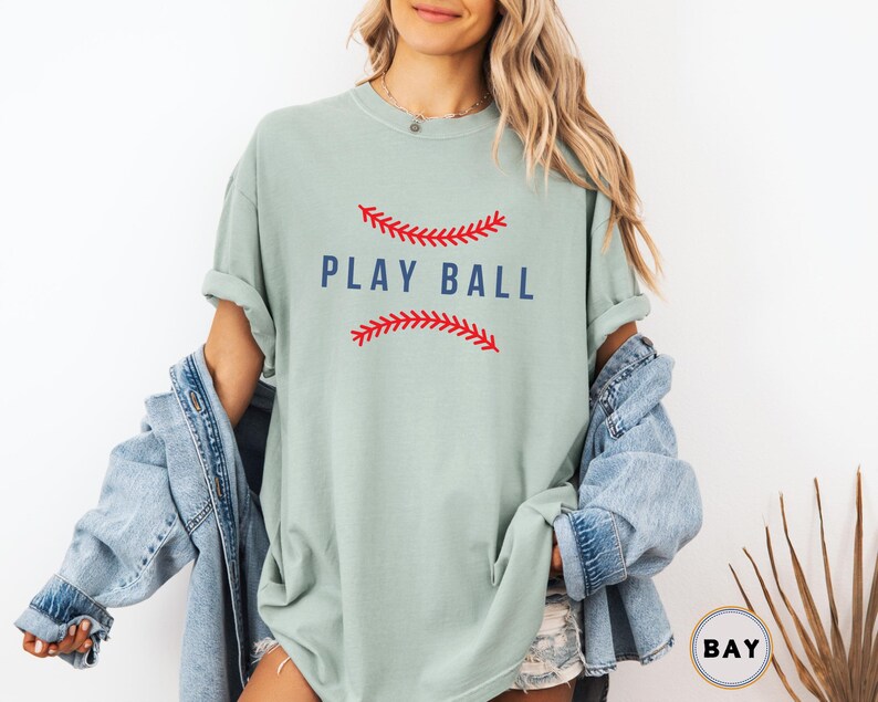 May include: A light green t-shirt with a red and white baseball graphic and the text "PLAY BALL" in blue.