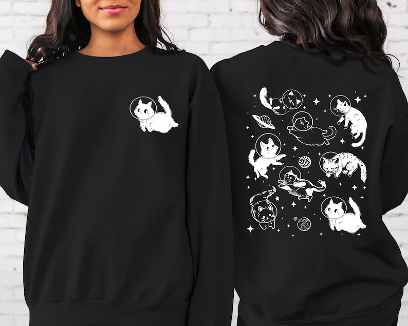 Peut inclure: Sweat-shirt noir avec un motif blanc de chats dans l'espace au dos et un seul chat dans l'espace sur le devant. Les chats portent des casques d'astronautes.