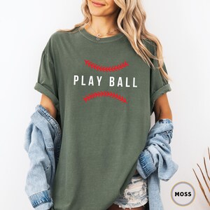 May include: A green t-shirt with a white graphic that says "Play Ball" with red stitching around the text.