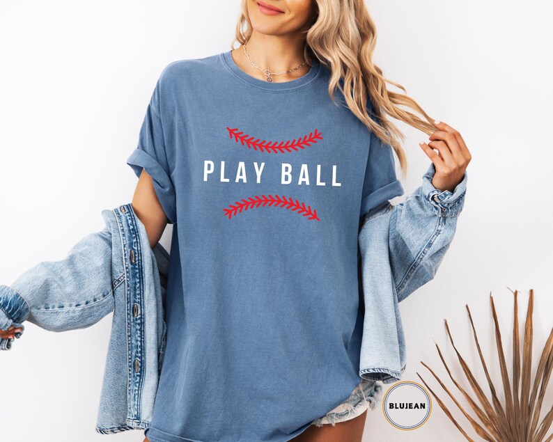 May include: A blue t-shirt with the text "PLAY BALL" in white letters. The text is surrounded by a red baseball stitch design.
