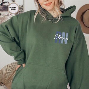 May include: A dark green hooded sweatshirt with the text "Elaina RN" in blue and white lettering.