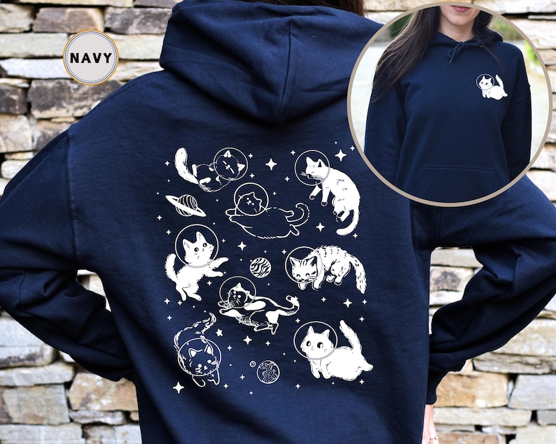 Peut inclure: Un sweat &agrave; capuche bleu marine avec un motif blanc de chats dans l'espace. Le motif repr&eacute;sente des chats en combinaison spatiale, des plan&egrave;tes et des &eacute;toiles. Le sweat &agrave; capuche a une capuche avec cordon de serrage et une poche kangourou.
