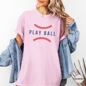 May include: Pink t-shirt with a red and white baseball graphic and the text "PLAY BALL" in blue.