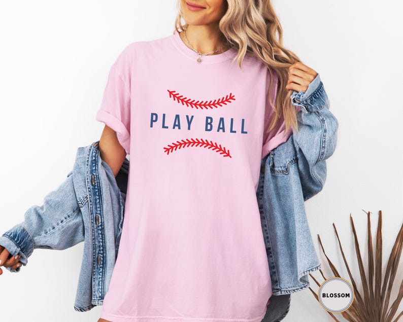May include: Pink t-shirt with a red and white baseball graphic and the text "PLAY BALL" in blue.