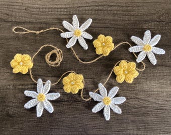 Puede incluir: Una guirnalda de flores de crochet blancas y amarillas enhebradas en una cuerda. Las flores están dispuestas en un patrón alterno.