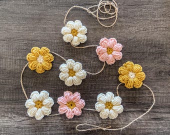 Puede incluir: Guirnalda de flores de ganchillo hechas a mano, con flores blancas, amarillas y rosas. Las flores están unidas con hilo natural, creando un elemento decorativo. Ideal para añadir un toque artesanal a cualquier espacio. Un artículo encantador y artesanal.