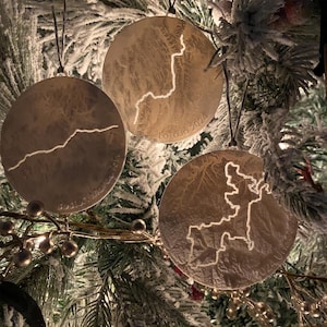 May include: Three round, silver-colored Christmas ornaments with a textured surface. Each ornament features a white outline of a map of a different region. The ornaments are labeled "Bosnia, May 2023", "Lotojo 2024", and "2023".