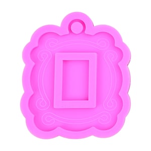 May include: Pink silicone mold shaped like a picture frame with a smaller rectangular cutout inside. The frame has a decorative design around the edges.
