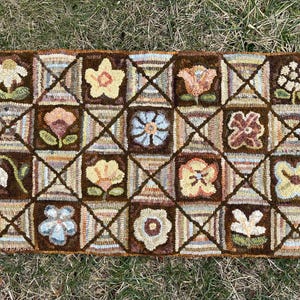 May include: A brown and beige hooked rug with a geometric pattern of squares and diamonds. Each square features a different floral design, including a variety of flowers, leaves, and stems.