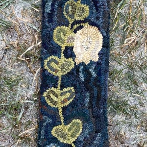 May include: A hand-hooked rug with a floral design. The rug is blue with white and yellow flowers and green leaves. The rug is rectangular and has a fringed edge.