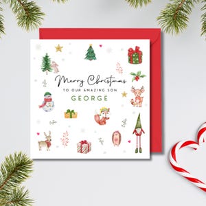 May include: A Christmas card with a red envelope. The white card features watercolor illustrations of festive elements like a snowman, fox, and presents. The text reads "Merry Christmas to our amazing son George."