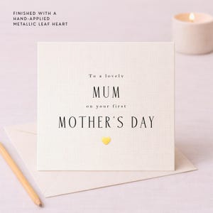 Puede incluir: Una tarjeta crema del Día de la Madre con las palabras "To a lovely MUM on your first MOTHER'S DAY" en texto negro. Un pequeño corazón amarillo está debajo del texto. La tarjeta está en un sobre crema.