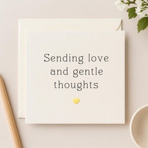 Peut inclure: Carte de vœux crème avec les mots "Sending love and gentle thoughts" en texte noir. Un petit cœur jaune est en dessous du texte. La carte est à l'intérieur d'une enveloppe crème.