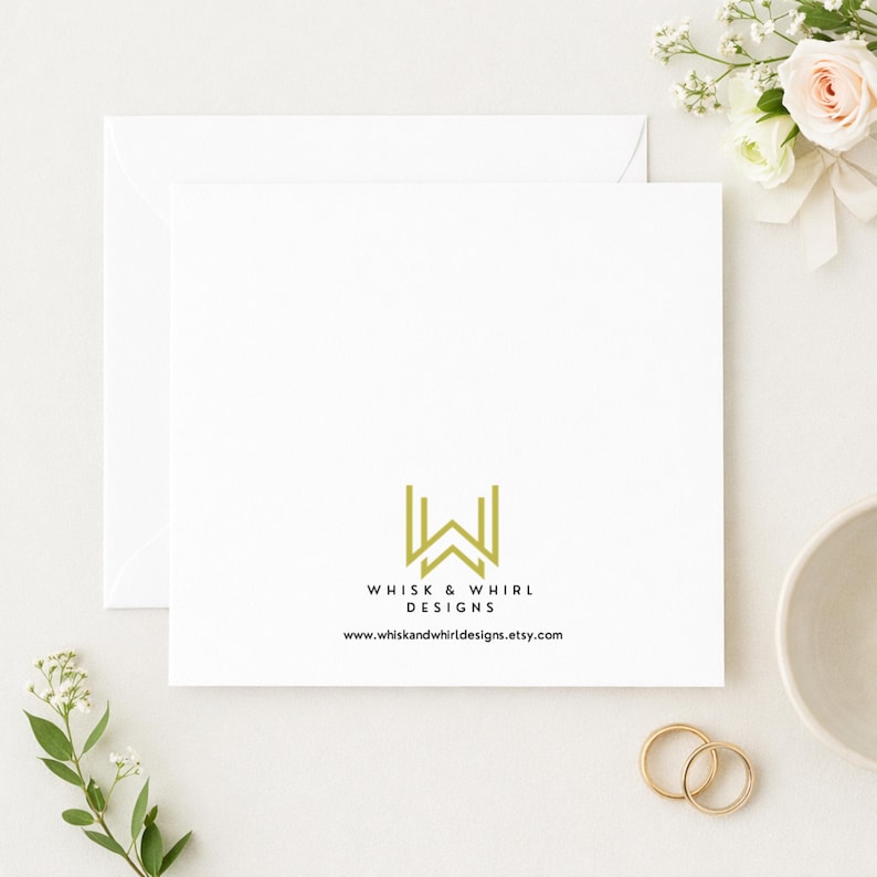 May include: A white square card with the text "WHISK & WHIRL DESIGNS" and a gold logo. The card is placed on a white surface with a white envelope, flowers, and two gold rings. The website address is also visible.