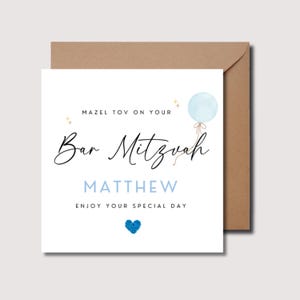 Pu&ograve; includere: Un biglietto bianco con un palloncino blu e stelle dorate. Il testo sul biglietto recita "Mazel Tov on your Bar Mitzvah Matthew Enjoy your special day".
