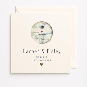 Puede incluir: Tarjeta de compromiso color crema con un mapa circular de Londres. La tarjeta presenta los nombres "Harper & Finley", la palabra "Engaged", la fecha "10 de junio de 2026" y un corazón dorado. Un sobre está detrás de la tarjeta.