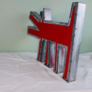 May include: A metal sign in the shape of a dog, with a red interior and a silver exterior. The sign is made of riveted metal and has a textured finish. The dog's silhouette is stylized and modern, suitable for home decor.