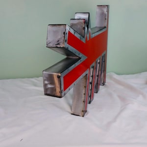 May include: A metal sculpture in the shape of a stylized Union Jack flag. The sculpture features a red and silver design with a textured, industrial aesthetic. The piece has a geometric, angular form.