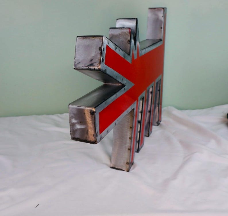 May include: A metal sculpture in the shape of a stylized Union Jack flag. The sculpture features a red and silver design with a textured, industrial aesthetic. The piece has a geometric, angular form.