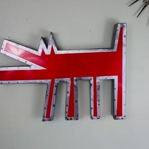 May include: A large, red metal dog-shaped wall art piece with a silver border and rivets. The dog has an open mouth and stylized legs. A mid-century modern starburst clock is visible in the background.
