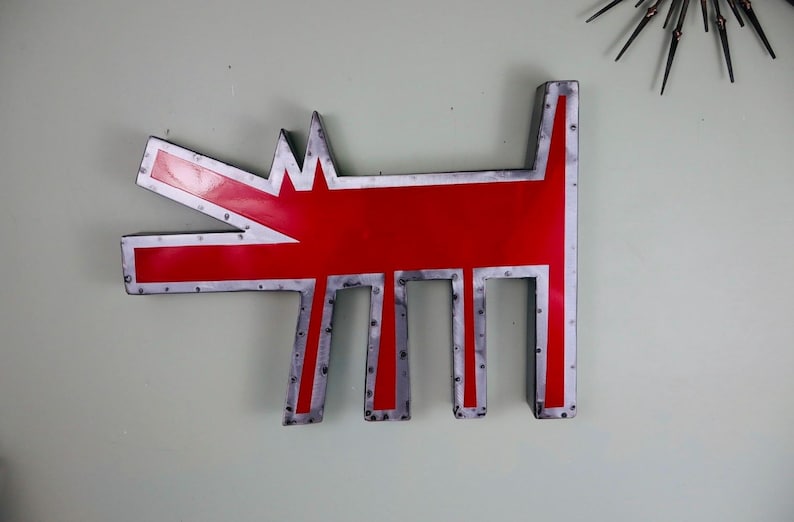 May include: A large, red metal dog-shaped wall art piece with a silver border and rivets. The dog has an open mouth and stylized legs. A mid-century modern starburst clock is visible in the background.