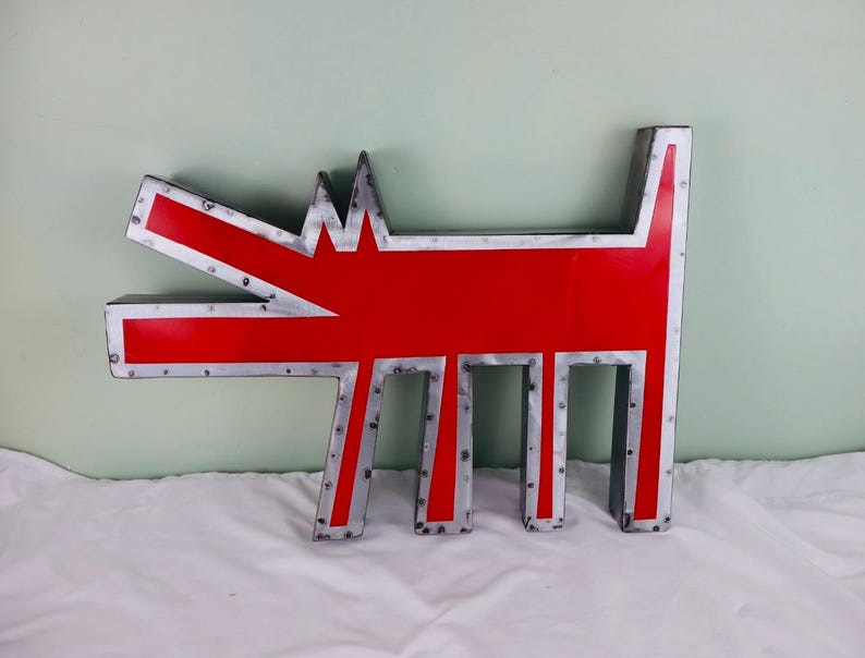 May include: A large, stylized metal dog sculpture. The dog is primarily red with silver-colored trim and rivets. The dog's mouth is open, and it has a jagged crown-like shape on its head. The sculpture is on a white surface.