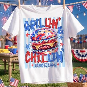 May include: A white short-sleeve t-shirt featuring a graphic of a burger with red, white, and blue star patterns. The text reads GRILLIN' & CHILLIN' SINCE 1776 in red and blue lettering, set against a background of light blue vertical stripes.