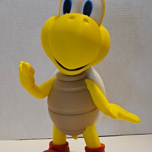 May include: A yellow and brown toy turtle with red shoes and blue eyes. The turtle is smiling and has a white shell.