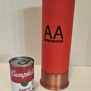 May include: A red and copper colored shotgun shell with the text "AA Winchester" printed on the side. A can of Campbell's Cream of Mushroom soup is in the foreground.