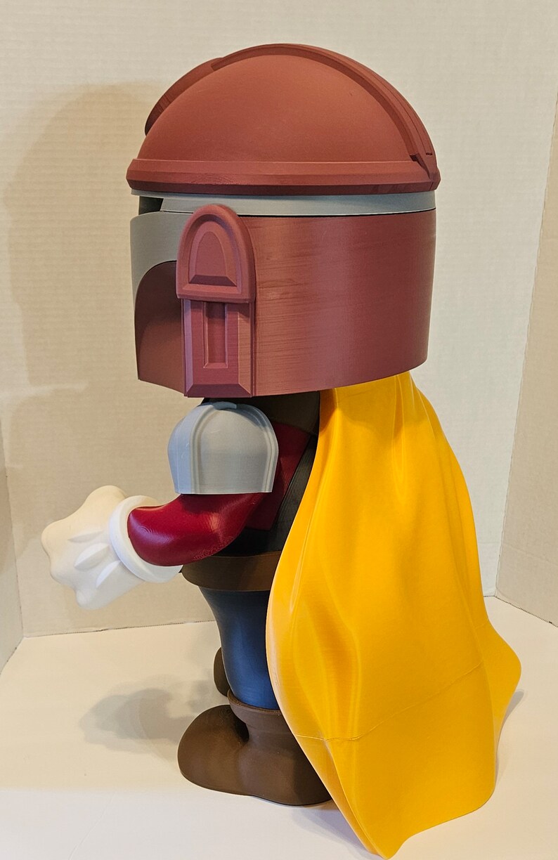 Op de afbeelding: Een 3D-geprint beeldje van een personage met een roodbruine helm, een gele cape en bruine laarzen. Het beeldje houdt een witte handschoen uit.