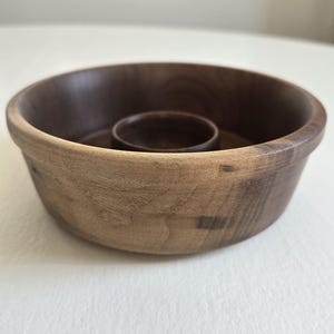 May include: A handcrafted wooden bowl with a central, smaller bowl. The exterior is a light brown, while the interior is a darker brown. The bowl has a smooth, rounded shape, perfect for serving snacks or displaying decorative items.