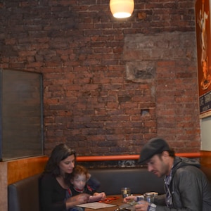 The glowing pendant hangs above a New York City corner booth with an exposed brick background.