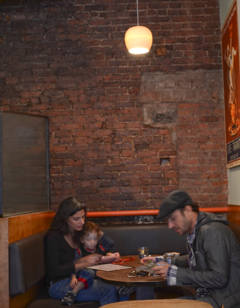 The glowing pendant hangs above a New York City corner booth with an exposed brick background.