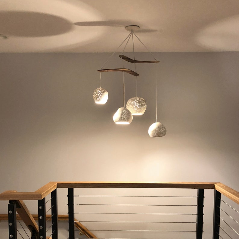 The boomerang large hangs illuminates a staircase. The wood and metal railings are a nice compliment to the curved wood and matte white ceramic shades, which appear to twinkly as light pours through the perforations.